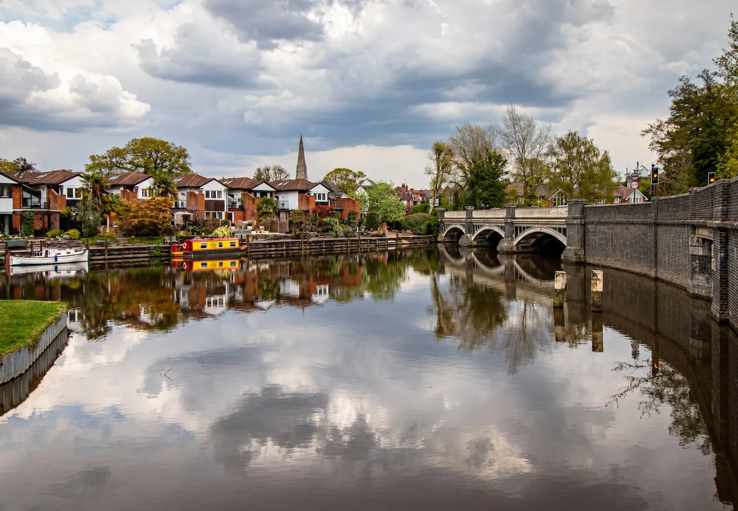 Weybridge river and arched stone bridge, with a church spire reflected in the water
